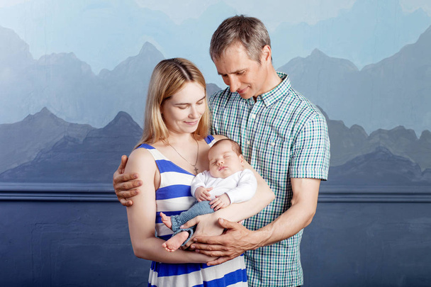 Woman and man holding a newborn. Mom, dad and baby.  Portrait of  smiling family with newborn on the hands. Happy family on a background. - Φωτογραφία, εικόνα