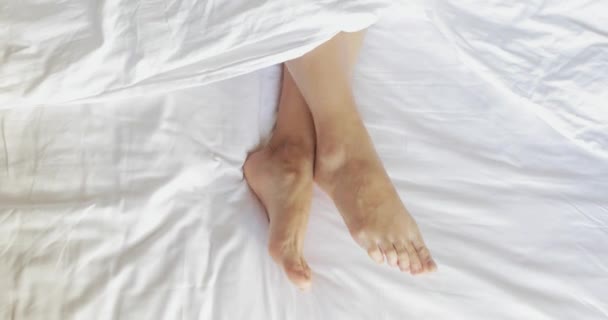 female legs in bed view from above, white bedding, 4k - Metraje, vídeo