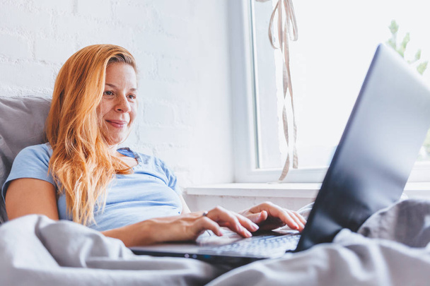 Woman working in bed on laptop early in the morning - Photo, Image