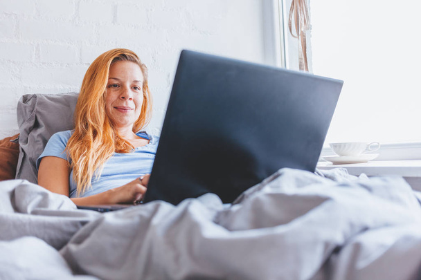 Frau arbeitet frühmorgens am Laptop im Bett - Foto, Bild