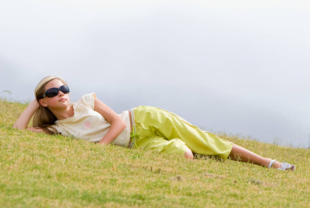 beautiful teen girl wearing sunglasses lying on green grass, full length  - Foto, imagen