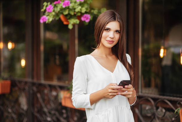 Cheerful female walking on city street enjoying free time on spring weekends holding smartphone for sending messages, happy woma using application on mobile - Zdjęcie, obraz
