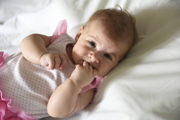 Baby girl holding her fingers in the mouth, looking to the camer - Foto, Bild