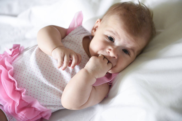 Baby girl holding her fingers in the mouth, looking to the camer - Photo, image