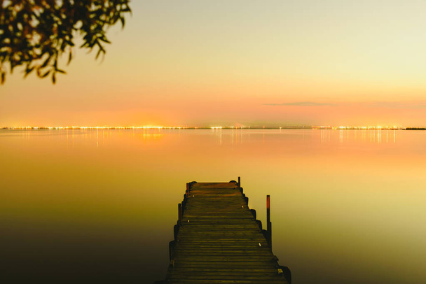 Molo na jezeře, při západu slunce s klidnou vodou a odrazy světílek. - Fotografie, Obrázek