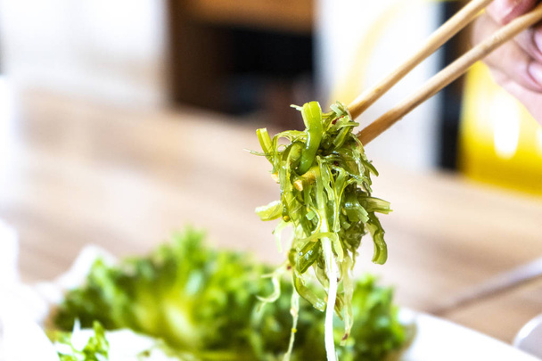 Japanese seaweed salad in chopstick  on hand 's man ready to eat. - Photo, Image