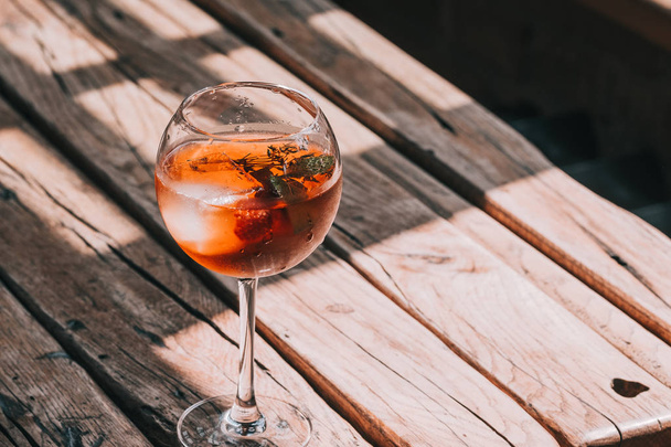 Aperol Spritz in wine glass on wooden table at the restaurant. Food photography. Direct sunlight, copyspace - Foto, imagen