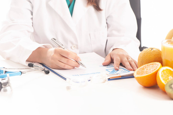 Nutritionist writing medical records and prescriptions with fresh fruits - Fotografie, Obrázek