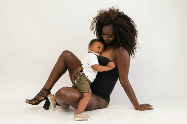 Atrakcyjne Afryki czarny młoda kobieta z małego synka siedzi na kolanach. Rodzina. - Zdjęcie, obraz
