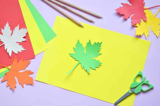 Making maple leaf from colored paper with your own hands for decoration of greeting card. Handmade crafts. Hello Autumn concept. Children's DIY. Copy space. Step 1. Circle the stencil - 写真・画像
