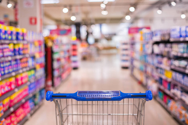 Προβολή καλαθιού στο διάδρομο Supermarket με ράφια προϊόντων αφηρημένη θολούρα αποπροσανατολισμένη φόντο - Φωτογραφία, εικόνα