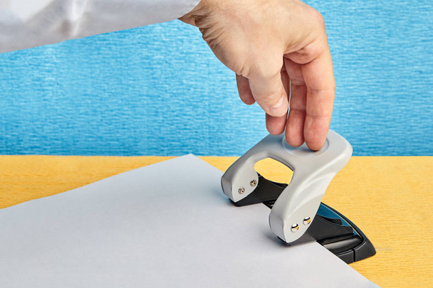 Hand presses on the office instrument  to make holes in the paper. - Foto, Bild