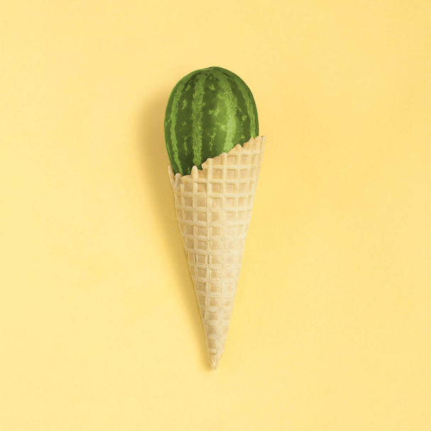 Mini melon with striped skin like watermelon in waffle cone on yellow background. Size of fruit is 2 inches. Hybrids, result of selection. Minimal style. Food concept of amazing fruits and desserts - Fotoğraf, Görsel