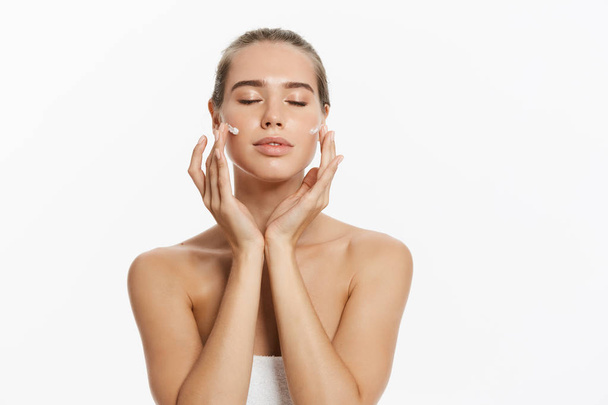 Mooie jonge vrouw cosmetische crème behandeling toe te passen op haar gezicht geïsoleerd op witte achtergrond - Foto, afbeelding