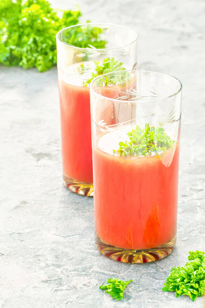 Two glasses of tomato juice homemade from garden organic vegetables decorated with twigs leaves of parsley and celery in table - Фото, зображення