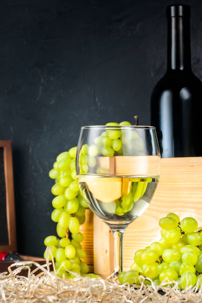 White wineglass and white yellow green bunches of berry grapes with bottle of wine corkscrew for cork on table in winery Concept food agriculture harvesting winemaking autumn summer. - Photo, Image
