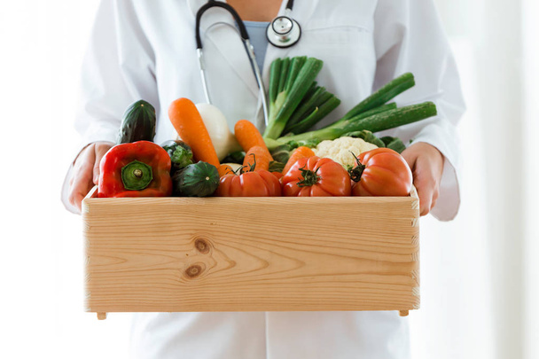 Close-up of nutritionist holding wooden box with fresh vegetables over white background. - Fotoğraf, Görsel