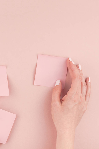 Kreatív lapos laikus fotó munkaterület íróasztallal ezeréves rózsaszín matrica papír modell, akár nő kezében tartja és ragasztás falon másol hely háttérstílusra minimális post. Szövegének sablonja - Fotó, kép