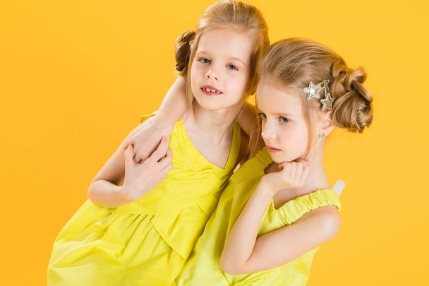 Twins girls are sitting on a chair on a yellow background. - Φωτογραφία, εικόνα
