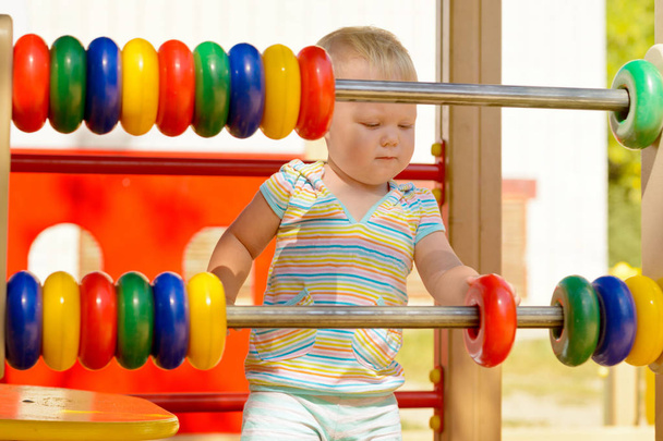 Egy kislány csíkos ruhát játszó gyermek műanyag gyűrű a játszótéren. Egy ragyogó napsütéses napon a kéz és a gondolkodás, a finom motoros készségek fejlesztéséhez - Fotó, kép