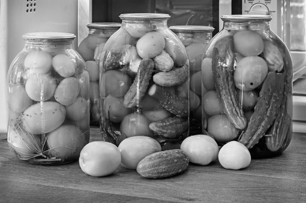 Huis van bewaring: grote glazen potten met rode rijpe tomaten en gepekelde komkommers, verzegelde metallid. Zwart-wit afbeelding. - Foto, afbeelding