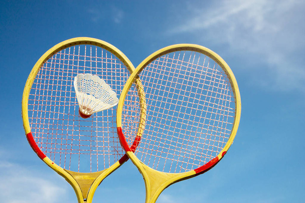 Two wooden badminton racket and shuttlecock flying against the blue sky and sun background - Fotografie, Obrázek