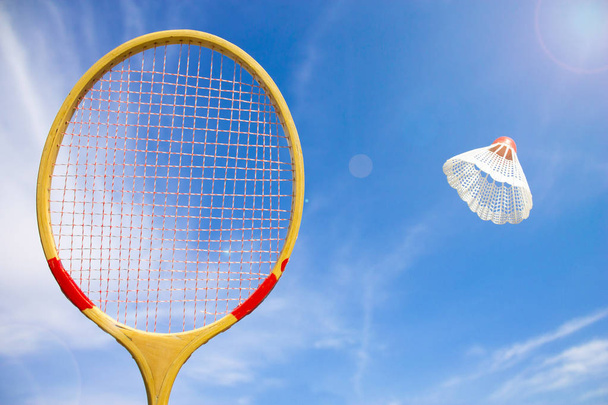 Wooden badminton racket and shuttlecock flying against the blue sky and sun background - Foto, imagen