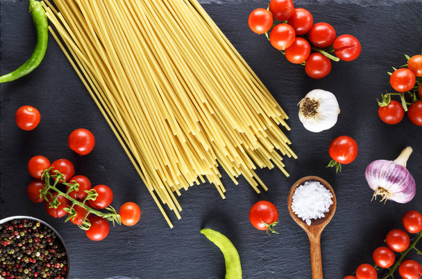 Spaghettis de pâtes non cuites sur fond noir, tomates cerises rouges et ail pour sauce, vue sur le dessus
 - Photo, image