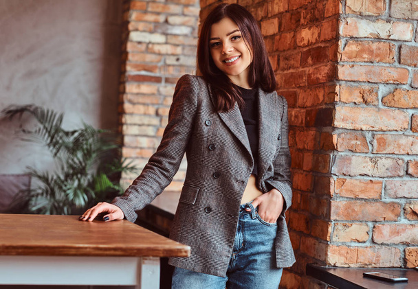 Happy sensual brunette woman dressed in trendy clothes posing in a room with loft interior, looking at camera. - Foto, imagen