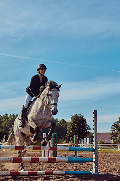 Giovane fantino femmina su dapple cavallo grigio saltare oltre ostacolo nell'arena aperta
. - Foto, immagini