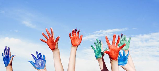 Happy children painted hands against blue summer sky background - Photo, Image