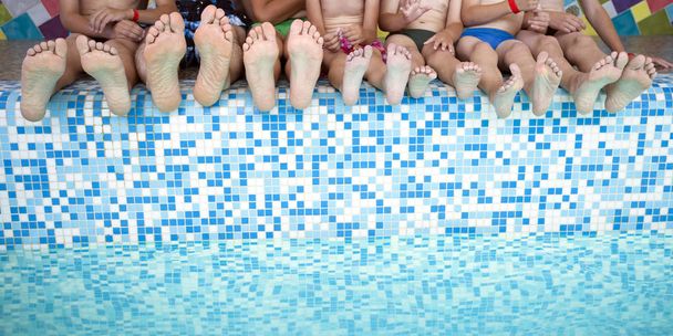 スイミング プールの端に座っている人の足のグループ。友人やスイミング プールの端に子供を持つ親のグループの足 - 写真・画像