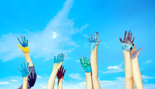 Happy children painted hands against blue summer sky background - Photo, Image
