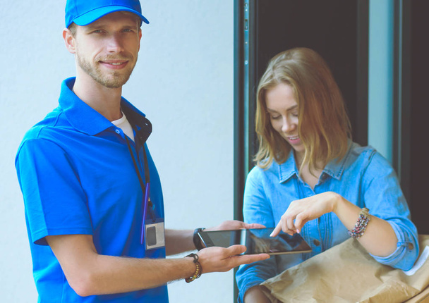 Smiling delivery man in blue uniform delivering parcel box to recipient - courier service concept - Fotografie, Obrázek