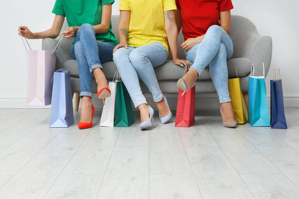 Group of young women with shopping bags sitting on sofa near light wall - Photo, Image