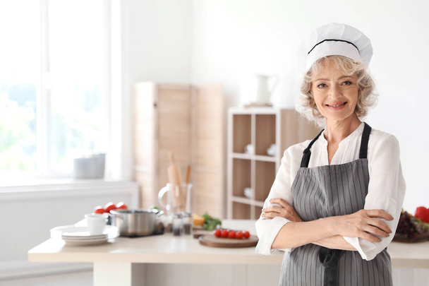 Professional female chef standing near table in kitchen - Foto, afbeelding