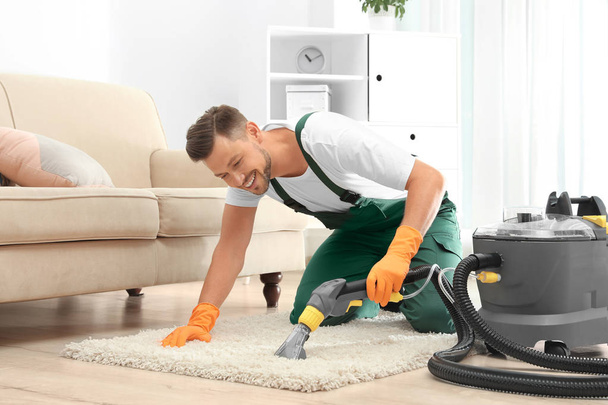 Male janitor removing dirt from rug with carpet cleaner in room - Fotó, kép