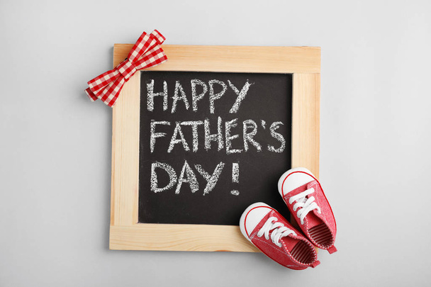 Flat lay composition with blackboard and baby shoes on gray background. Happy Father's Day - Фото, изображение