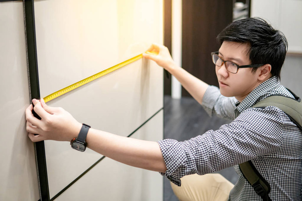 ウォークイン クローゼット ショールームでモダンなキャビネットを測定用巻尺を使って若い男性。ホーム改善のための家具のショッピング。インテリア デザインのコンセプト - 写真・画像