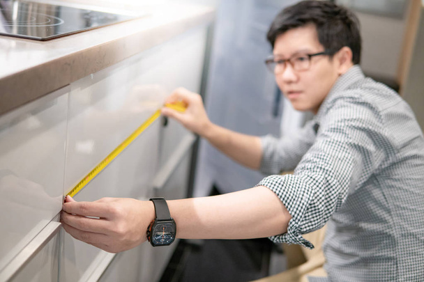 Giovane uomo asiatico utilizzando metro a nastro per misurare moderno bancone della cucina in showroom. Mobili per la casa concetto di miglioramento dello shopping
 - Foto, immagini