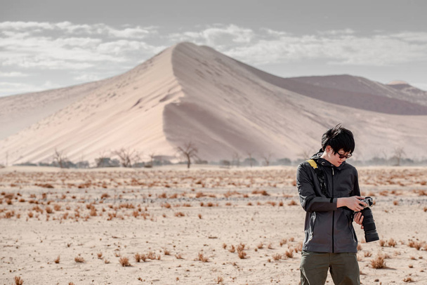 Jeune voyageur et photographe regardant l'affichage de photos sur l'appareil photo dans le désert de Namib avec une dune de sable en arrière-plan. Voyage Namibie, Afrique. Concept de photographie
 - Photo, image