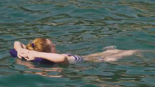 Nainen ilman meikkiä lepää. Tyttö kelluu meressä selällään makaamassa puhallettavalla tyynyllä. 4K hidastus
 - Materiaali, video