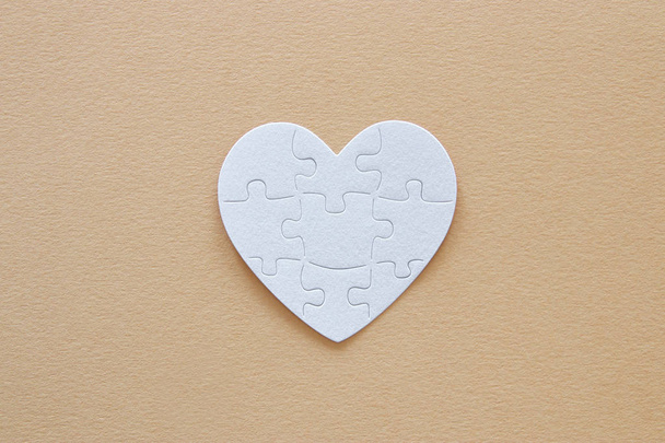Top view image of paper white heart puzzle over brown pastel background. Health care, donate, world heart day and world health day concept - Фото, изображение