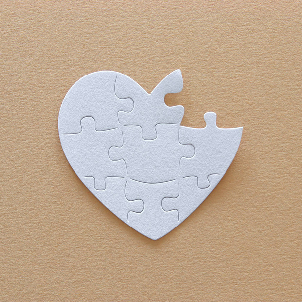 Top view image of paper white heart puzzle with missing piece over brown pastel background. Health care, donate, world heart day and world health day concept - Foto, Imagen