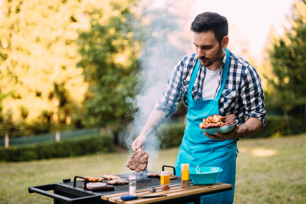 Happy male grilling bbq meat outdoor in nature - Fotó, kép