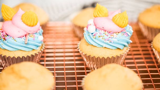 一歩一歩。ユニコーン buttercream のフロスティングは虹をテーマにしたバニラカップ ケーキを飾る. - 写真・画像
