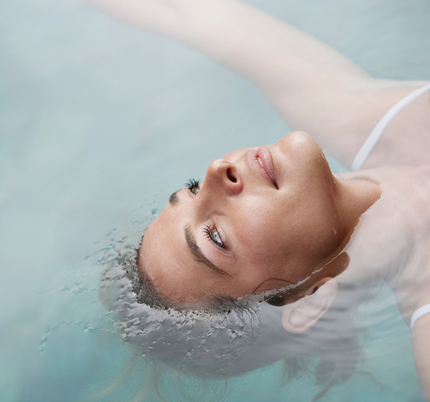 κοντινό πλάνο πάνω από το κεφάλι προβολή μιας νεαρής γυναίκας που επιπλέει στο νερό ενώ σε μια πισίνα στις διακοπές. - Φωτογραφία, εικόνα