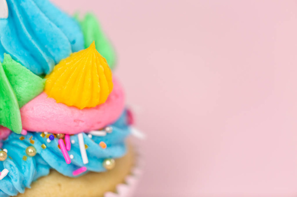 Fancy unicorn cupcakes met multicolor botterroom slagroom en unicorn cupcake topper op roze achtergrond. - Foto, afbeelding