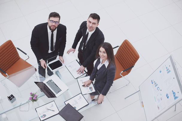 top view.business team stands near the desktop and looks at the camera - Fotografie, Obrázek