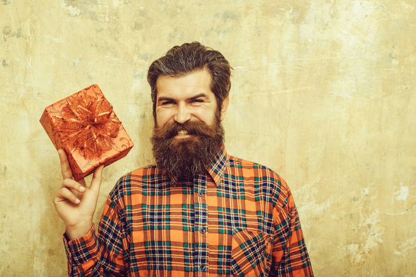 Happy bearded man smiling with red gift box with bow - Zdjęcie, obraz